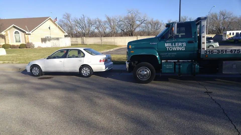 Miller's Towing truck parked beside a white sedan for a jump start in a Wichita neighborhood