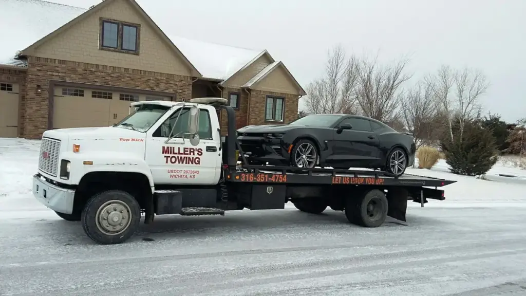 Miller's Towing flatbed hauling a black sports car on a snowy Wichita street